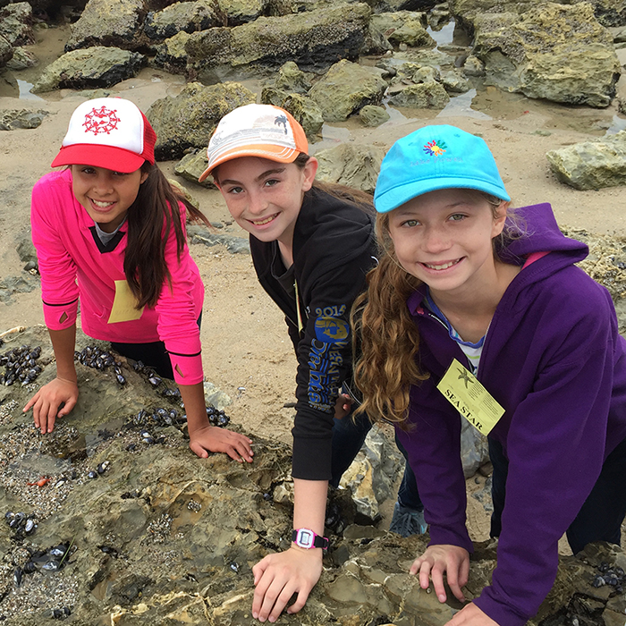 three girls leaning on rock in tidepools